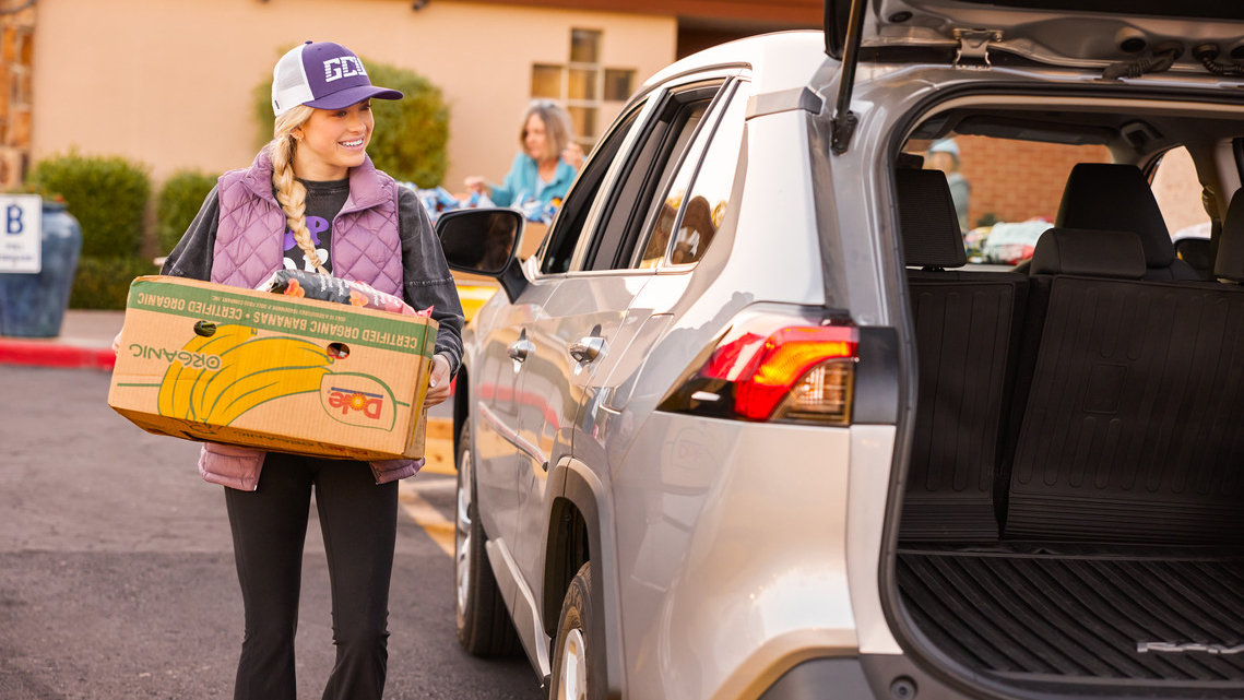 Blonde girl in GCU attire volunteers at local food bank putting box of food in back of an SUV